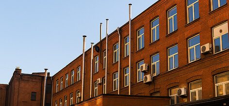 Brick building with lots of windows and ACs bolted on the walls, empty flagpoles out front, blue sky overhead—real straightforward.